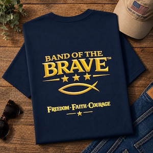 May include: A navy blue t-shirt featuring the yellow text BAND OF THE BRAVE with three stars, a fish symbol, and the words FREEDOM FAITH COURAGE below it. The design includes a small star at the bottom, all printed in a bold, gold-toned font.