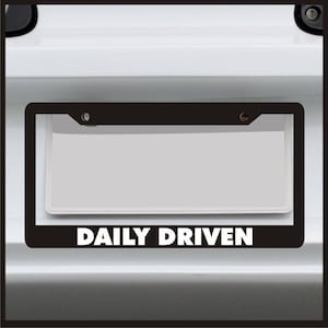 May include: Black license plate frame with the text "DAILY DRIVEN" in white letters.