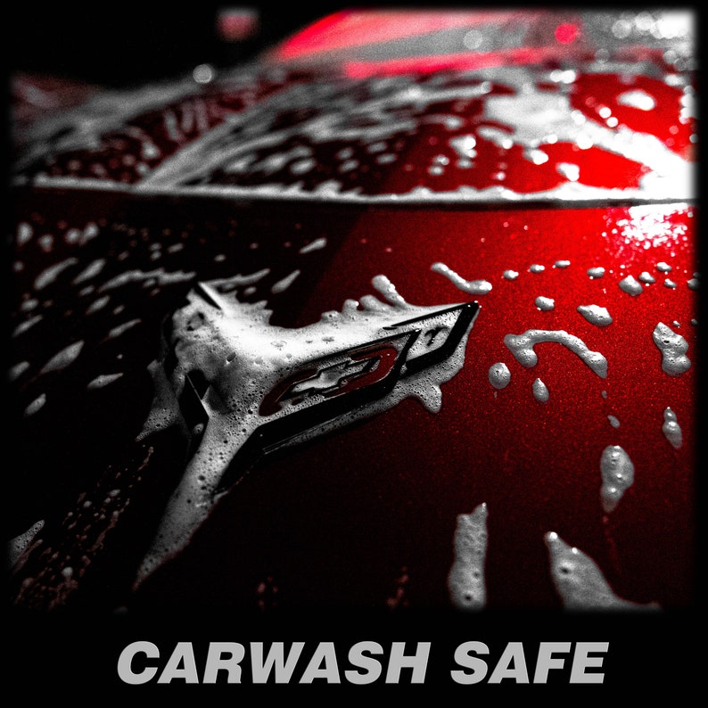 Może przedstawiać: Czerwony samoch&oacute;d z białą pianą pokrywającą maskę. Emblemat samochodu jest widoczny przez pianę. Tekst "CARWASH SAFE" jest wydrukowany pod obrazem.