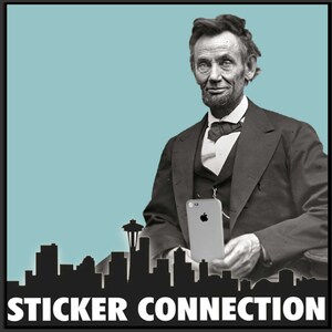 Może przedstawiać: Czarno-białe zdjęcie Abrahama Lincolna trzymającego smartfona przed panoramą Seattle w stanie Waszyngton. Na dole zdjęcia widnieje napis "STICKER CONNECTION".
