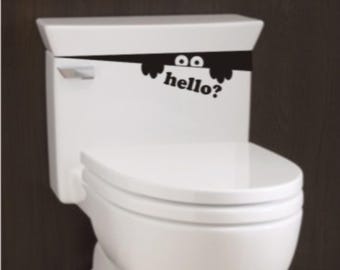May include: White toilet with a black and white sticker on the tank that says "hello?" with two eyes peeking out from behind the sticker.