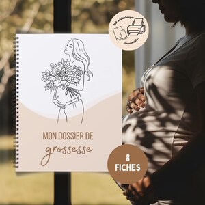 Może przedstawiać: Spiralnie oprawiony notatnik z rysunkiem kobiety w ciąży trzymającej kwiaty. Okładka zawiera napis "MON DOSSIER DE grossesse" w ozdobnej czcionce. Małe k&oacute;łko z napisem "8 FICHES". Obraz zawiera r&oacute;wnież grafikę telefonu, tabletu i drukarki.