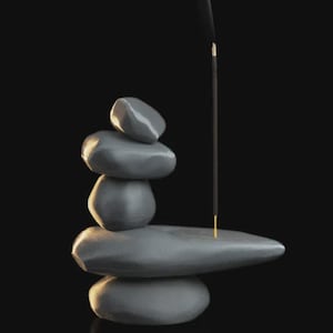 May include: A stack of smooth, gray stones with an incense stick emitting smoke against a black background. The stones are arranged in a balanced tower, with the incense stick placed in a holder on top. The overall aesthetic is minimalist and zen-like.