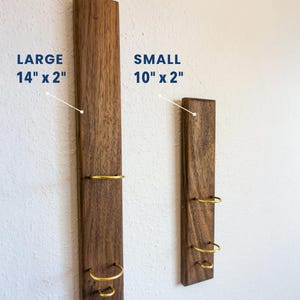 May include: Two wooden wall-mounted wine racks. The larger rack is 14 inches long and 2 inches wide, and the smaller rack is 10 inches long and 2 inches wide. Each rack has three gold-colored metal rings.