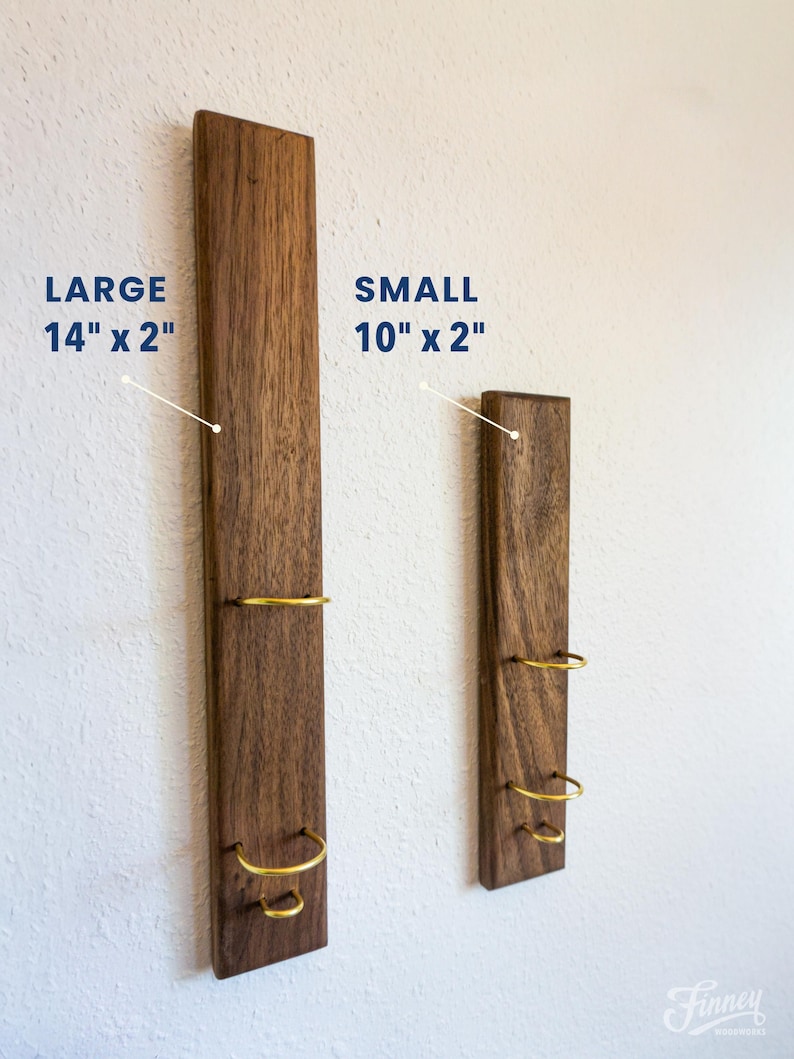May include: Two wooden wall-mounted wine racks. The larger rack is 14 inches long and 2 inches wide, and the smaller rack is 10 inches long and 2 inches wide. Each rack has three gold-colored metal rings.