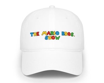 May include: A white baseball cap featuring the text THE MARIO BROS. SHOW printed in a multi-colored, blocky font across the front panel. The letters are colored in red, yellow, blue, and green, and the cap has a curved brim and a button top.