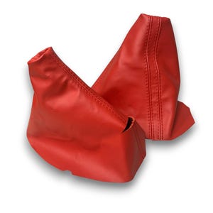 May include: Two bright red leather shift boots, likely for a vehicle's gear shift lever. The boots are made of a smooth material and have stitched seams. The boots are displayed against a white background.