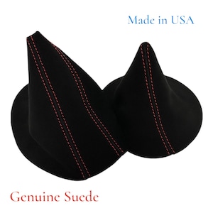 Puede incluir: Dos piezas de ante negro con costuras rojas. El texto "Made in USA" está encima de los objetos y "Genuine Suede" debajo. Las piezas tienen forma de cono con base circular.