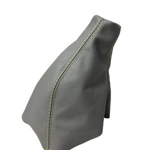 May include: A gray leather car shift boot with yellow stitching. The boot is made of a textured material and has a curved shape. The stitching runs along the seams of the boot.