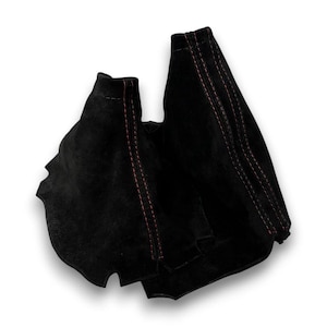 May include: A black suede gear shift boot featuring prominent red stitching along the seams. The fabric is textured with a matte finish, and the design includes structured panels joined by the red thread, creating a tapered, conical shape.