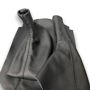 May include: Black leather shift boot with visible stitching. The boot has a textured surface and a cylindrical top. The design appears to be for a vehicle's gear shift lever. The leather is a deep, solid black.