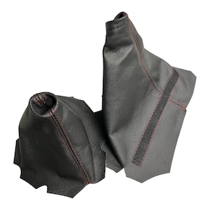 May include: Two black leather shift boots with red stitching. The word "Manual" is in a red box in the upper left corner. The shift boots are designed to cover the gear shift lever in a vehicle.