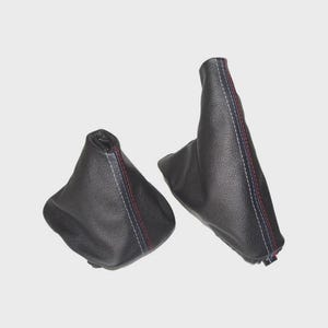 May include: Two black leather shift boots with red, white, and blue stitching. The boots are made of a textured leather material and are designed to fit over a vehicle's gear shift lever. The boots are shown against a white background.