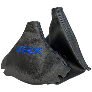Può includere: Una cuffia per leva del cambio nera testurizzata con cuciture blu e il testo ricamato in blu WRX. La cuffia presenta un design conico con una base ampia e un'apertura superiore stretta, che mette in risalto una lavorazione dettagliata.
