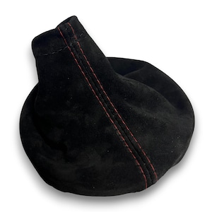 Könnte beinhalten: Ein schwarzer Schalthebelstiefel aus Wildleder mit roten Nähten. Der Stiefel hat eine weiche, abgerundete Form mit einem leicht ausgestellten Oberteil. Die roten Nähte verlaufen vertikal entlang der Naht.