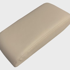 May include: A beige, rectangular padded armrest with rounded corners. The armrest has a stitched seam running down the center. The surface appears to be smooth leather or a leather-like material.