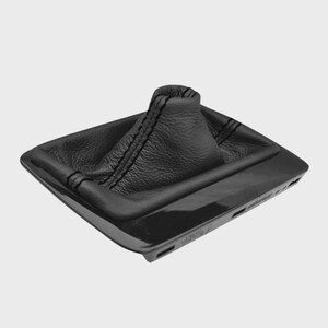 May include: A black leather shift boot with black stitching, set in a glossy black plastic base. The boot has a textured surface and a square shape, designed for a vehicle's gear shift.