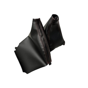 Könnte beinhalten: Zwei schwarze Schalthebelmanschetten mit roten Nähten. Die Manschetten haben ein Kohlefaser-Muster und bestehen aus einem strukturierten Material. Sie sind für die Montage am Schalthebel eines Fahrzeugs konzipiert.
