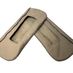 May include: Two beige leather car seat armrest covers. Each cover has a rectangular window and is stitched with dark thread. The covers are designed to protect the armrests from wear and tear.