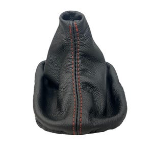 May include: A black leather gear stick gaiter with red stitching. The gaiter has a textured surface and a conical shape, designed to cover the gear stick in a vehicle. The red stitching runs vertically down the centre.