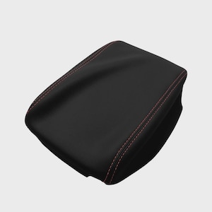 Puede incluir: Funda de reposabrazos de coche de cuero negro con costuras rojas. La funda es rectangular con bordes redondeados y una superficie lisa. Las costuras rojas proporcionan un detalle de contraste.
