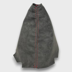 May include: A gray suede shift boot with red stitching down the center. The boot has a cone-like shape and is designed to cover the gear shift lever in a vehicle. The stitching is visible and adds a contrasting detail to the boot.
