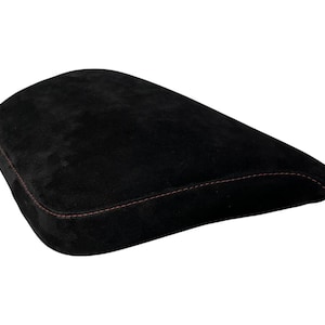 May include: A black suede-textured cushion with a curved, ergonomic shape. The edges of the cushion are defined by visible, contrasting dark red stitching that follows the perimeter of the object, highlighting its structured, tapered design.