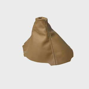 May include: A tan leather gear shift boot featuring a smooth, matte finish and prominent light-colored stitching along the vertical seams. The conical-shaped automotive interior component has a wide, scalloped base and a narrow, open top opening.