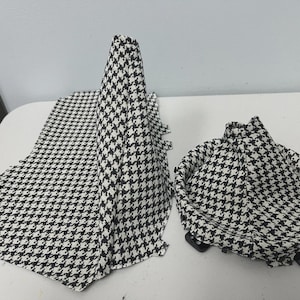 May include: A black and white houndstooth pattern fabric is arranged on a white surface. The fabric is draped in a scarf-like shape, a tall cone, and a small hat-like shape. The fabric is a classic, timeless design.