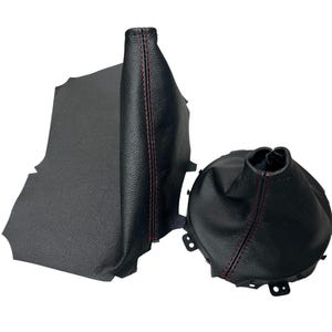 Peut inclure: Un soufflet de levier de vitesses et un cache de pommeau de levier de vitesses en cuir noir avec des coutures rouges. Le soufflet est rectangulaire et le cache est rond. Accessoires automobiles.