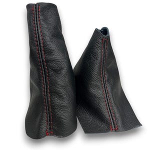 May include: Two black leather shift boots with red stitching. The boots are made of textured leather and have a cone-like shape. The red stitching is visible along the seams, adding a contrasting detail to the design.