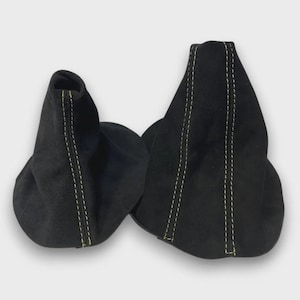 May include: Two black suede-like shift boots with yellow stitching. The boots are side-by-side, with a rounded bottom and a tapered top. The stitching runs vertically along the seams. The background is a solid, light gray.