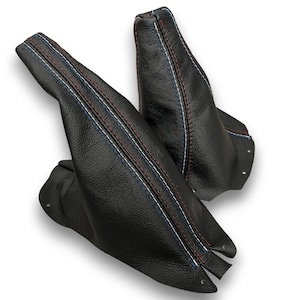May include: Two black leather gear stick gaiters with red, white, and blue stitching. The gaiters are made of textured leather and have a classic design. The stitching runs along the seams.