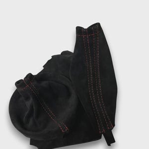 Könnte beinhalten: Schwarzer Wildlederstiefel mit roten Nähten. Der Stiefel hat eine runde Spitze und ein Design zum Anziehen. Die Nähte sind an den Nähten und um den oberen Teil des Stiefels sichtbar. Der Stiefel ist aus einem weichen, geschmeidigen Material gefertigt.