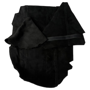 Puede incluir: Una prenda de cuero de gamuza negra, posiblemente un chaleco o accesorio, con una superficie texturizada. El artículo está doblado y tiene costuras visibles a lo largo de las costuras. La forma general es irregular, con un acabado oscuro y mate.