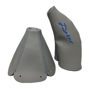 May include: Two grey leather gear shift boots with blue stitching. One boot has the word "Dakar" embroidered in blue. The boots are made of a smooth, durable material and are designed to protect the gear shift.