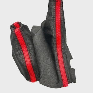 May include: Black leather car shift boot with a vibrant red stripe down the center. The boot is made of textured leather and has red stitching. The design is a sporty and stylish upgrade for a vehicle's interior.