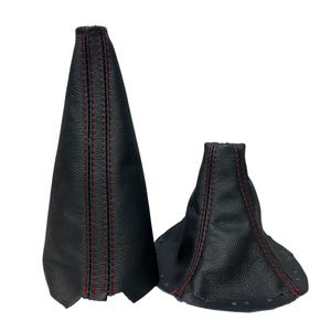 May include: Two black leather shift boots with red stitching. One boot is tall and conical, the other is shorter and flared. The leather has a textured appearance, and the stitching is visible along the seams.