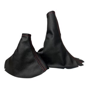 May include: Two black leather shift boot covers with red stitching. The covers are cone-shaped and appear to be made of a textured material. The red stitching provides a contrasting detail to the black leather.
