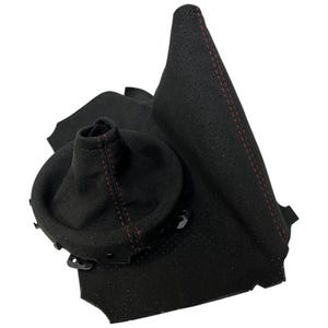 Könnte beinhalten: Eine schwarze Schalthebelmanschette für Kraftfahrzeuge aus perforiertem Material mit roten Nähten. Die Manschette verfügt über eine kreisförmige Öffnung an der Oberseite und eine strukturierte Basis mit sichtbaren Kunststoff-Befestigungsclips.