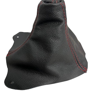 May include: Black leather shift boot with red stitching. The boot has a textured surface and a flared shape. The stitching follows the seams of the boot, creating a contrasting visual element. The boot is designed to fit around a gear shift.