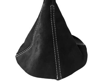 May include: A black, cone-shaped shift boot made of a suede-like material. The boot features white stitching along the seams, creating a contrasting detail. The design is simple and modern, suitable for automotive interiors.