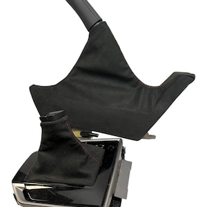 May include: A black car interior component set, including a parking brake handle and a gear shift boot. The gear shift boot is black with red stitching. The parking brake handle is black.