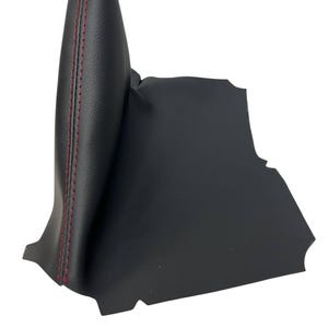 Puede incluir: Fuelle de palanca de cambios de coche de cuero negro con costuras rojas. Este accesorio automotriz está diseñado para proteger la palanca de cambios. Las costuras rojas contrastan con el cuero negro liso.