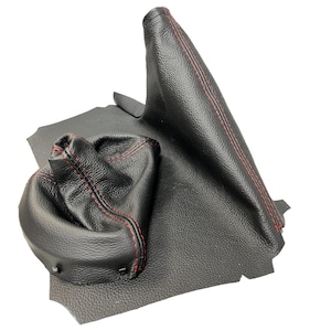 May include: Black leather car shift boot and parking brake boot with red stitching. The shift boot is a rounded shape, and the parking brake boot is a tall, tapered shape. Both are made of textured leather.