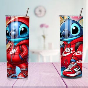 May include: Two stainless steel tumblers featuring a cartoon character in a red Nike tracksuit. The character is blue with large black eyes. The tumblers have a silver straw and a silver lid. The background is blurred.