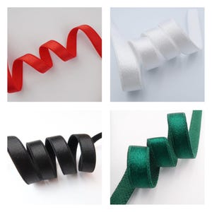 May include: Four samples of satin ribbon in red, white, black, and green. Each ribbon is curled and displayed against a white background. The ribbons are smooth and have a slight sheen, suggesting they are made of a high-quality material.