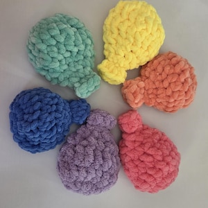 May include: A collection of six balloon-shaped items crafted from soft, chunky yarn in a variety of solid colors including mint green, bright yellow, peach, royal blue, lavender, and pink, each featuring a small knotted base and textured surface.