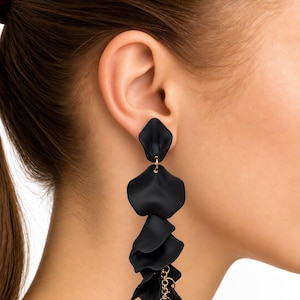 May include: A long, dangling earring featuring multiple matte black, petal-shaped components linked together. The top piece is a single petal, followed by a cascading series of layered black petals connected by small, thin gold-toned metal rings.