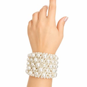 May include: A wide cuff bracelet composed of multiple rows of round, lustrous white faux pearls of varying sizes. The pearls are densely packed together to create a textured, multi-layered appearance that wraps around the wrist in a solid band.